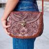Close-up of brown tooled leather shoulder bag worn by girl in bluejeans